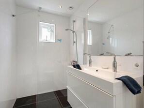 A modern bathroom with a glass shower enclosure, a large mirror, and a white vanity with a towel.