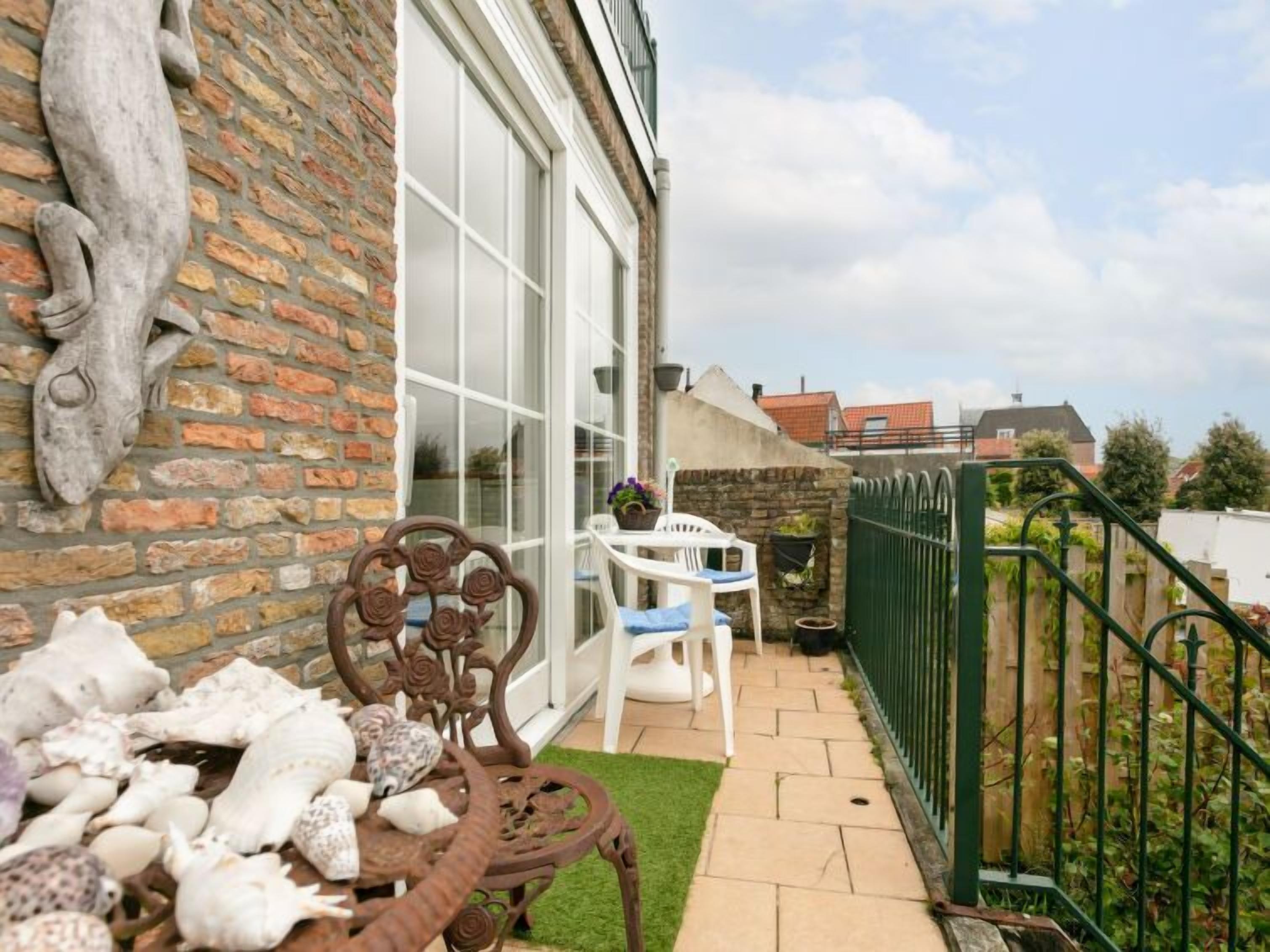 A patio with a brick wall, a white door, and a green metal fence.