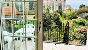 A view from a balcony with a table and chairs, a metal fence, and a historic building with large windows in the background.