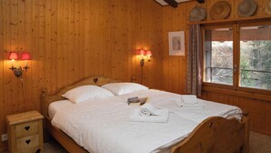 Ein hölzernes Himmelbett mit weißen Leinen, zwei Nachttischlampen, ein kleiner Nachttisch mit Schublade und ein Fenster mit Vorhängen.