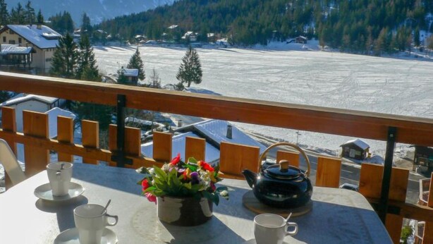Ein Balkon mit Tisch für zwei Personen, einer Teekanne und einer Blumenvase.