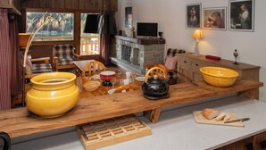 Eine rustikale Küche mit Holzmöbeln, einem großen gelben Topf, einem schwarzen Wasserkocher und einem Holztisch mit Brot und Schneidebrett.