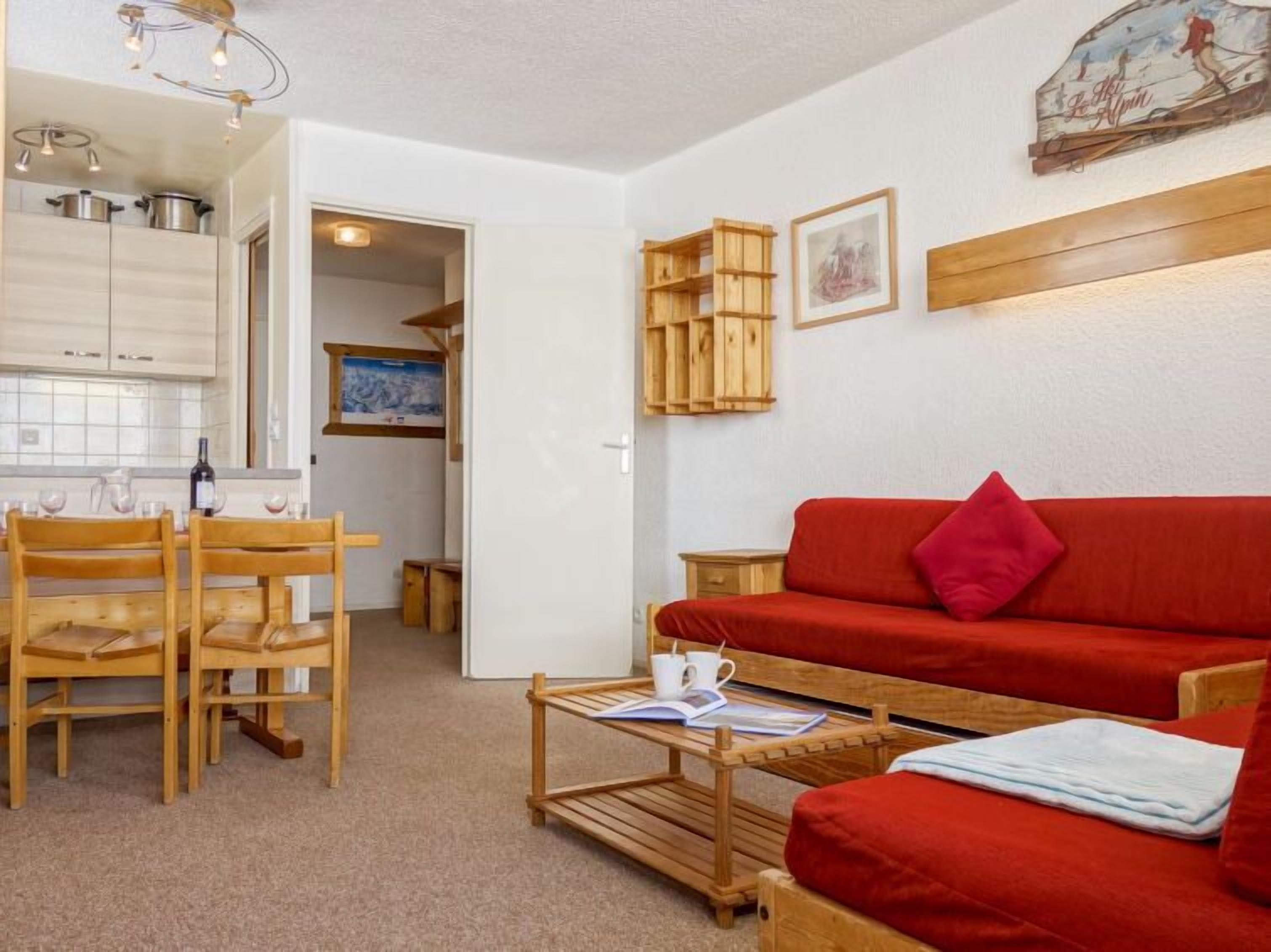 A compact living space with a dining area, a red sofa, and a small table with a book and a cup.