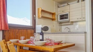 A wooden dining table with benches, a kitchen with white cabinets, a microwave, and a window with a view of mountains. - Les Tommeuses (Val Claret) by Interhome (Tignes)