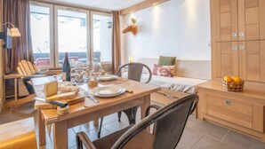 Ein Essbereich mit einem Holztisch, gedeckt für vier Personen, einer Couch mit Kissen und einer kleinen Sitzecke mit Orangen.