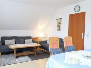 A cozy living room with a sofa, a coffee table, and two chairs. There's a wooden door and a wall clock.