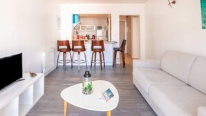 A modern living room with a white sofa, a white coffee table, and a TV on a white stand. There is a kitchen in the background with a dining area. - Résidence de France by Interhome (Saint-Jean-de-Luz)