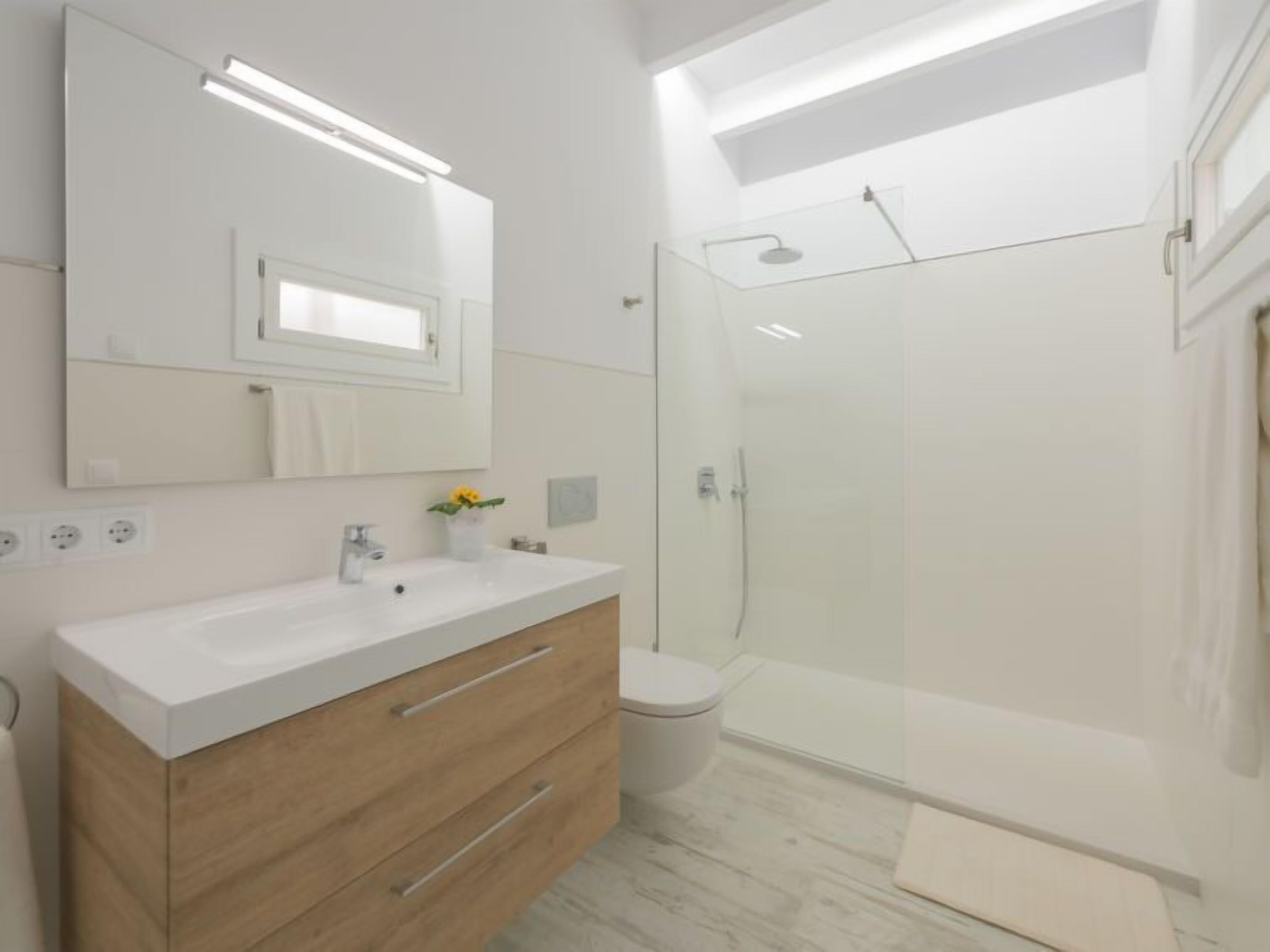 Et moderne badeværelse med et hvidt toiletbord, en glasbrusekabine og et stort spejl.