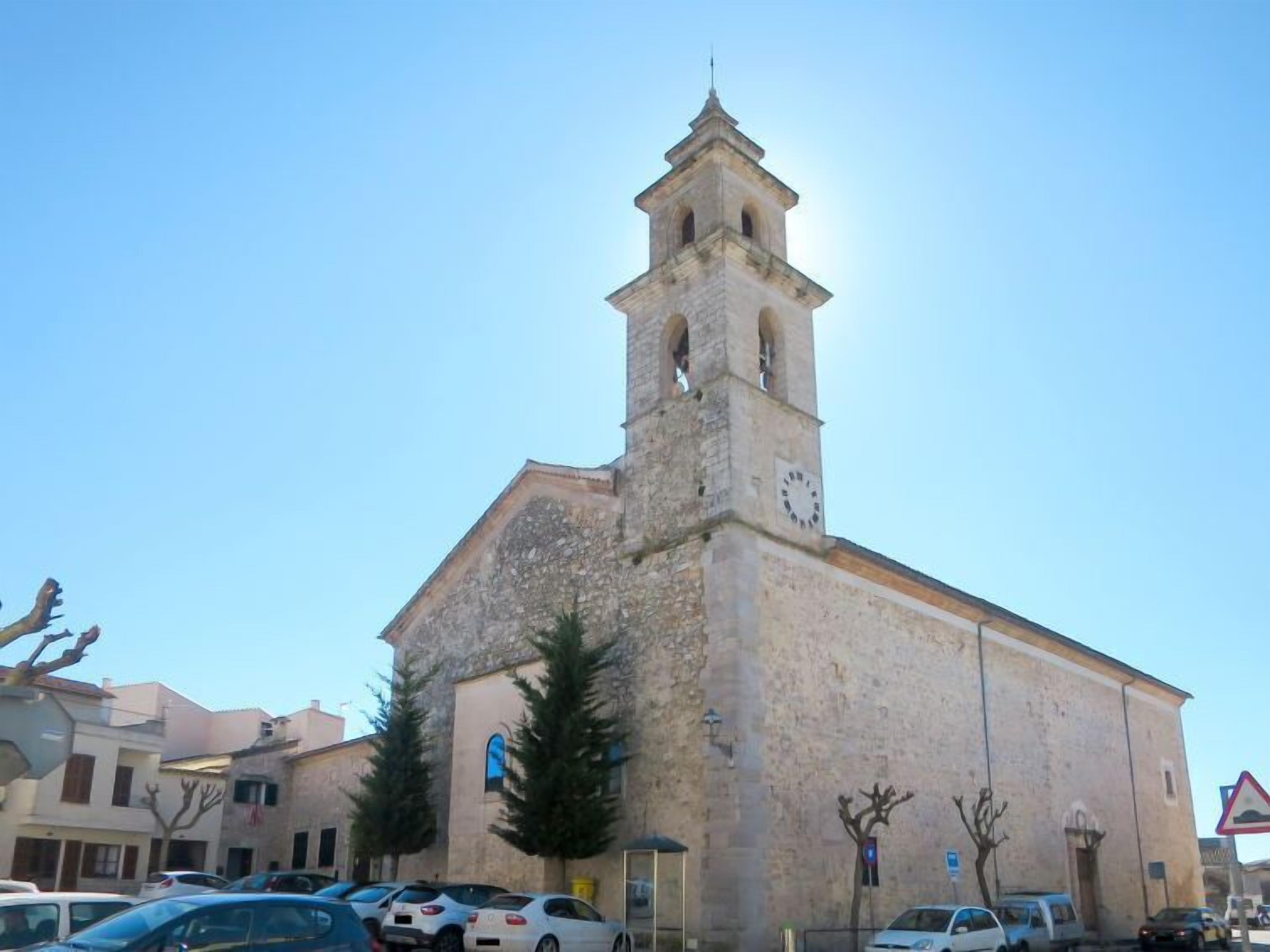 A historic stone church with a bell tower, surrounded by parked cars and residential buildings.
