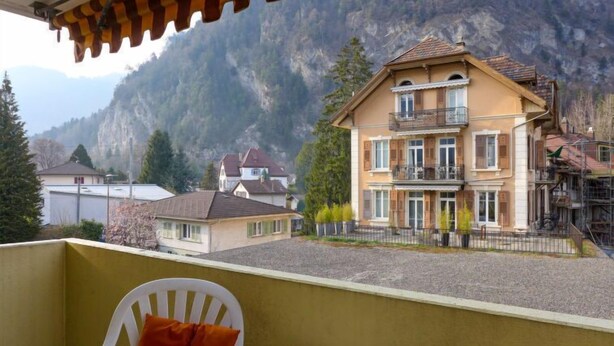 Un balcón con vista a una montaña y un edificio grande de dos pisos con balcones.