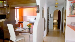 Una cocina moderna con armarios color naranja, un comedor con mesa y sillas blancas, y un pasillo que conduce a otra habitación.