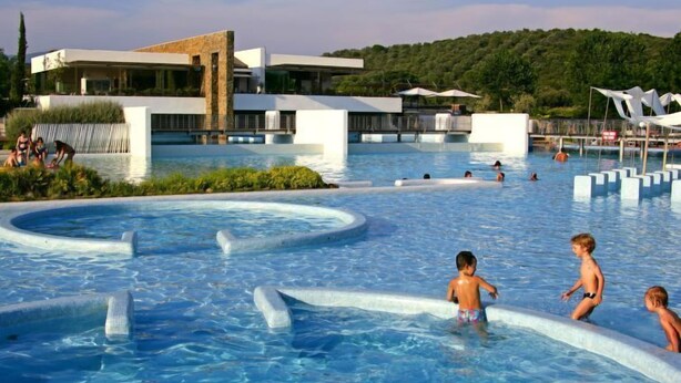 A modern pool area with clear water, surrounded by a building with a flat roof and large windows.