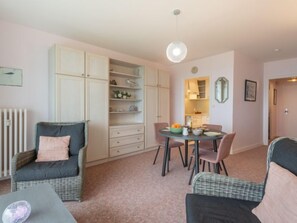 A cozy living room with a sofa, a dining table with chairs, and a large open shelving unit.