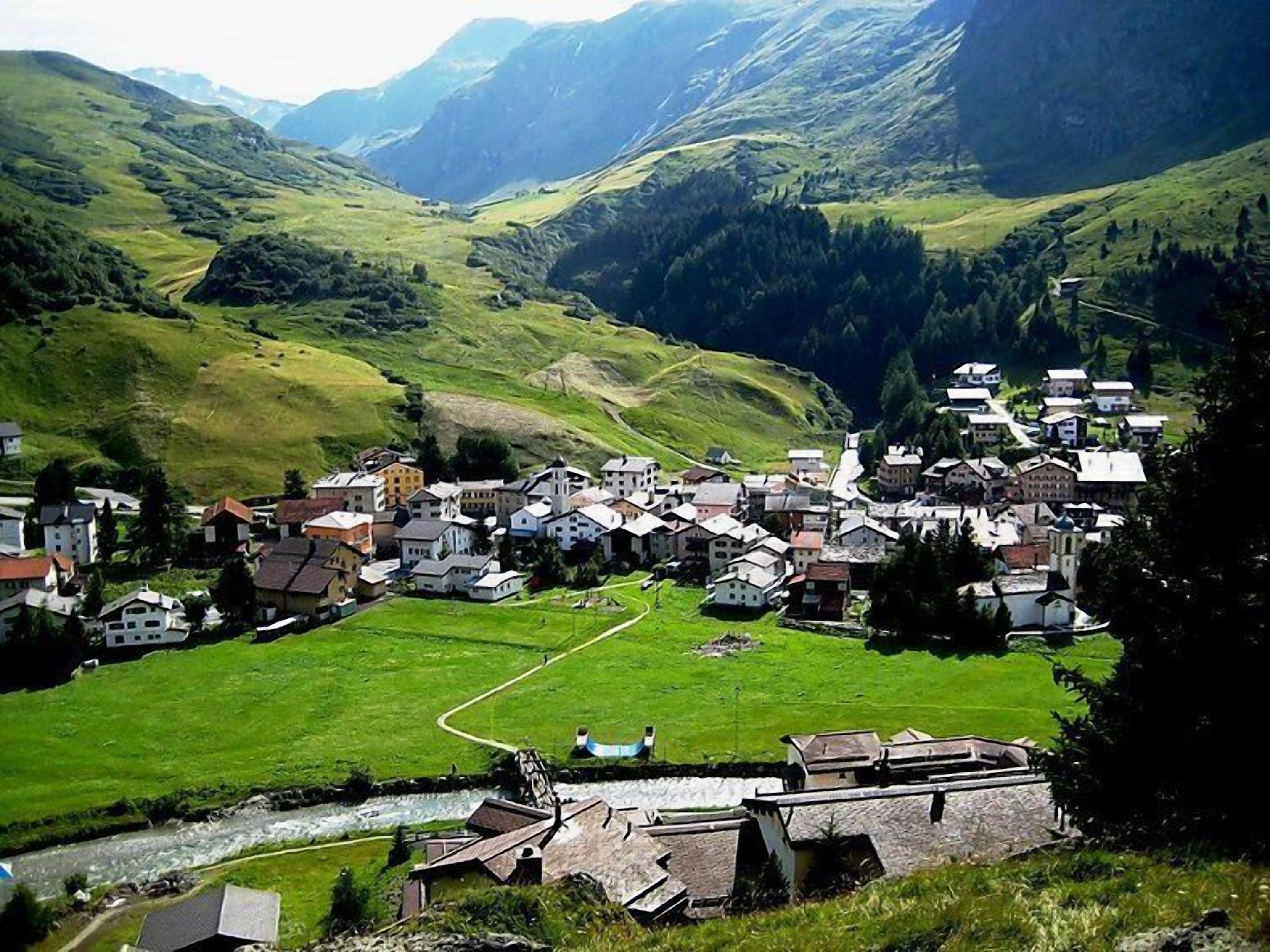 Ein Dorf mit traditionellen Häusern, einem Fluss und Bergen im Hintergrund.