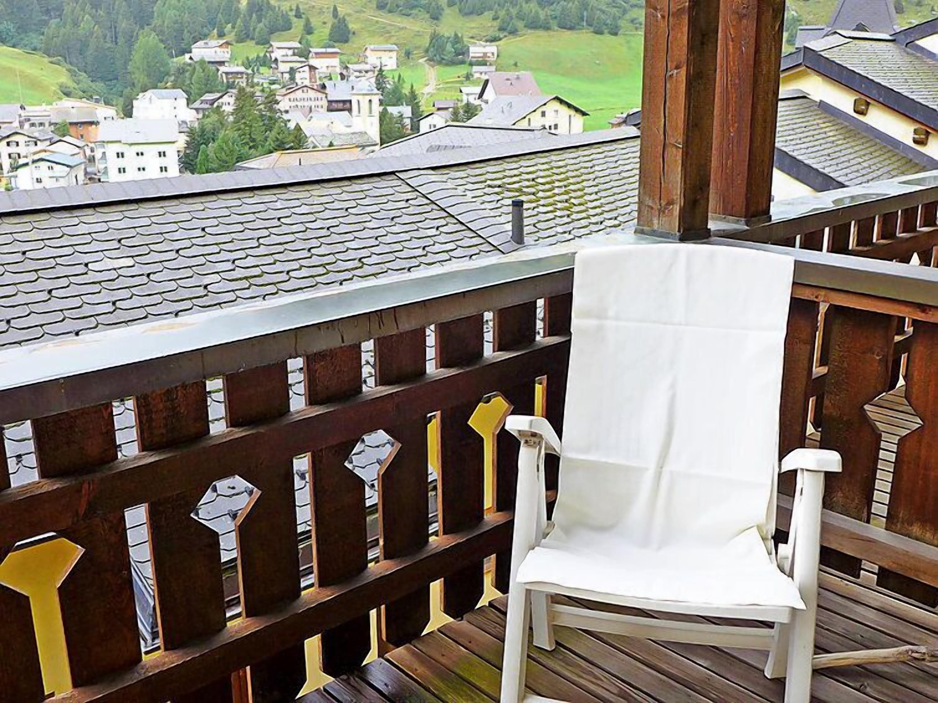 Una silla blanca sobre una terraza de madera con vistas a un pueblo con casas tradicionales.
