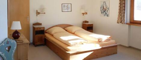 A bedroom with a wooden bed, bedside tables, a lamp, a chair, and a window with curtains.