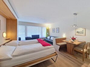 A hotel room with a bed, a desk, a chair, a sofa, and a window with blinds.