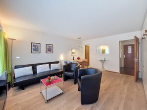 A modern living room with a sofa, chairs, a small table with fruit, and artwork on the walls.