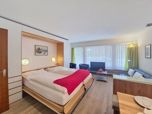 A hotel room with a bed, a desk, a chair, a television, and a window with curtains. - Matten (Utoring) by Interhome (Zermatt)