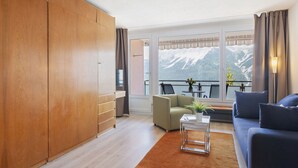 Ein modernes Wohnzimmer mit einem Holzschrank, einer Couch, einem Couchtisch und Bergblick durch große Fenster.