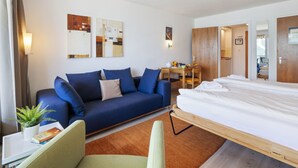 Ein modernes Hotelzimmer mit einer Couch, einem kleinen Tisch mit Pflanze, einem Bett und Kunstwerken an den Wänden.