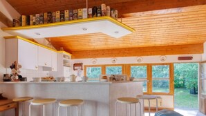 Uma cozinha acolhedora com vigas de madeira, um espaço de bar com banquetas e janelas amplas com vista para o verde.