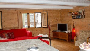 Ein gemütliches Wohnzimmer mit einem roten Sofa, einem Fernseher auf einem Holzschrank und einem Esstisch mit einer Schüssel Snacks.