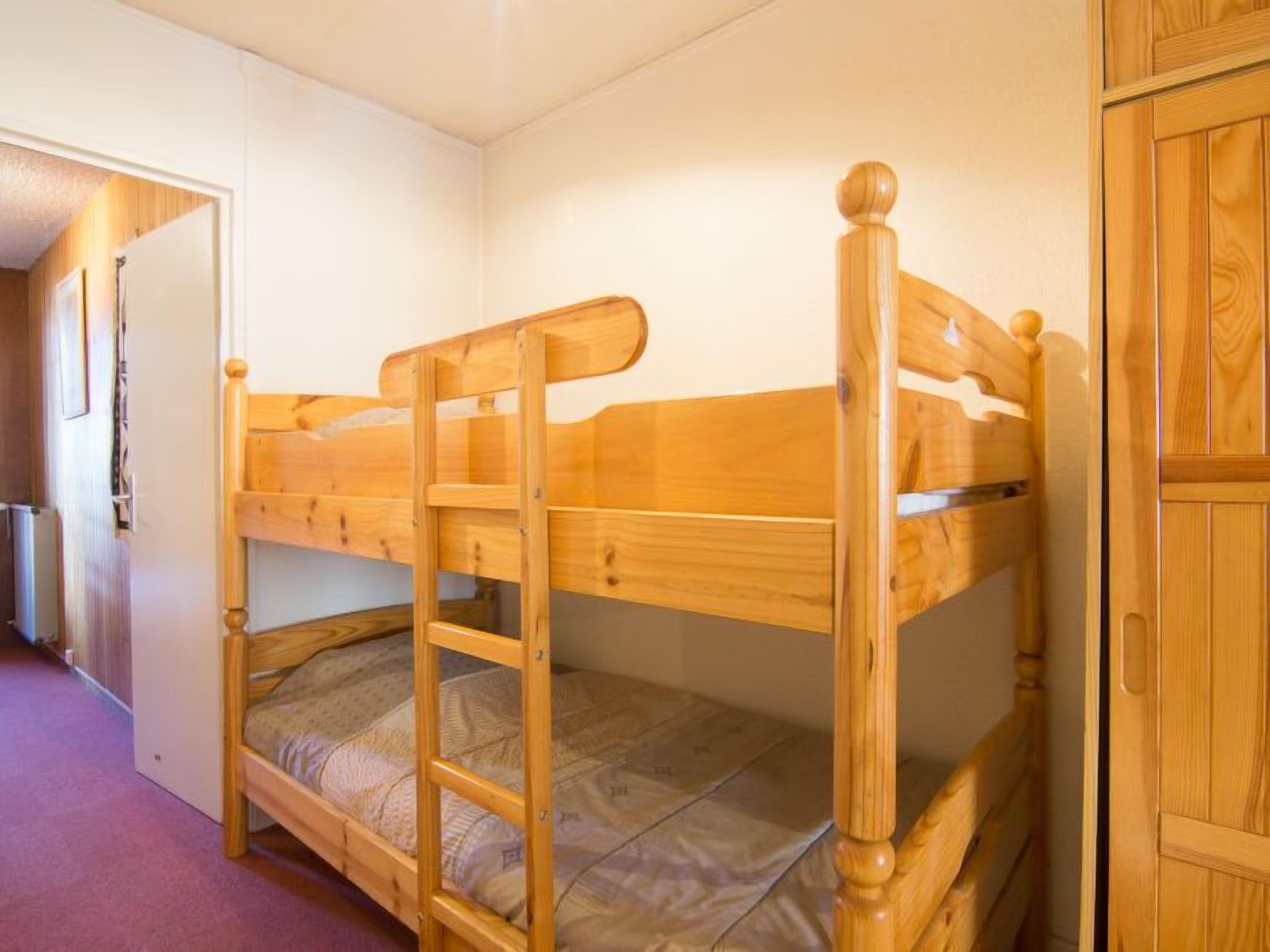 Une chambre avec un lit superposé, une échelle en bois, une porte et une armoire.