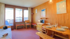 A cozy room with wooden walls, a dining table set for two, a bench, and a TV. - Le Curling B (Val Claret) by Interhome (Tignes)