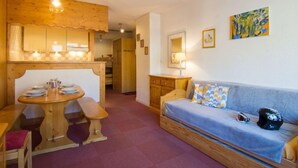 A cozy room with a wooden dining table, bench, and a sofa with cushions. There is a painting on the wall and a lamp on a bedside table. - Le Curling B (Val Claret) by Interhome (Tignes)