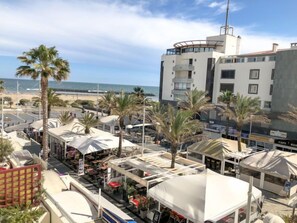 A coastal area with outdoor seating under umbrellas, a beach in the background, and a modern building with balconies. - Le Sunset/Cap Sud by Interhome (Cap d'Agde)