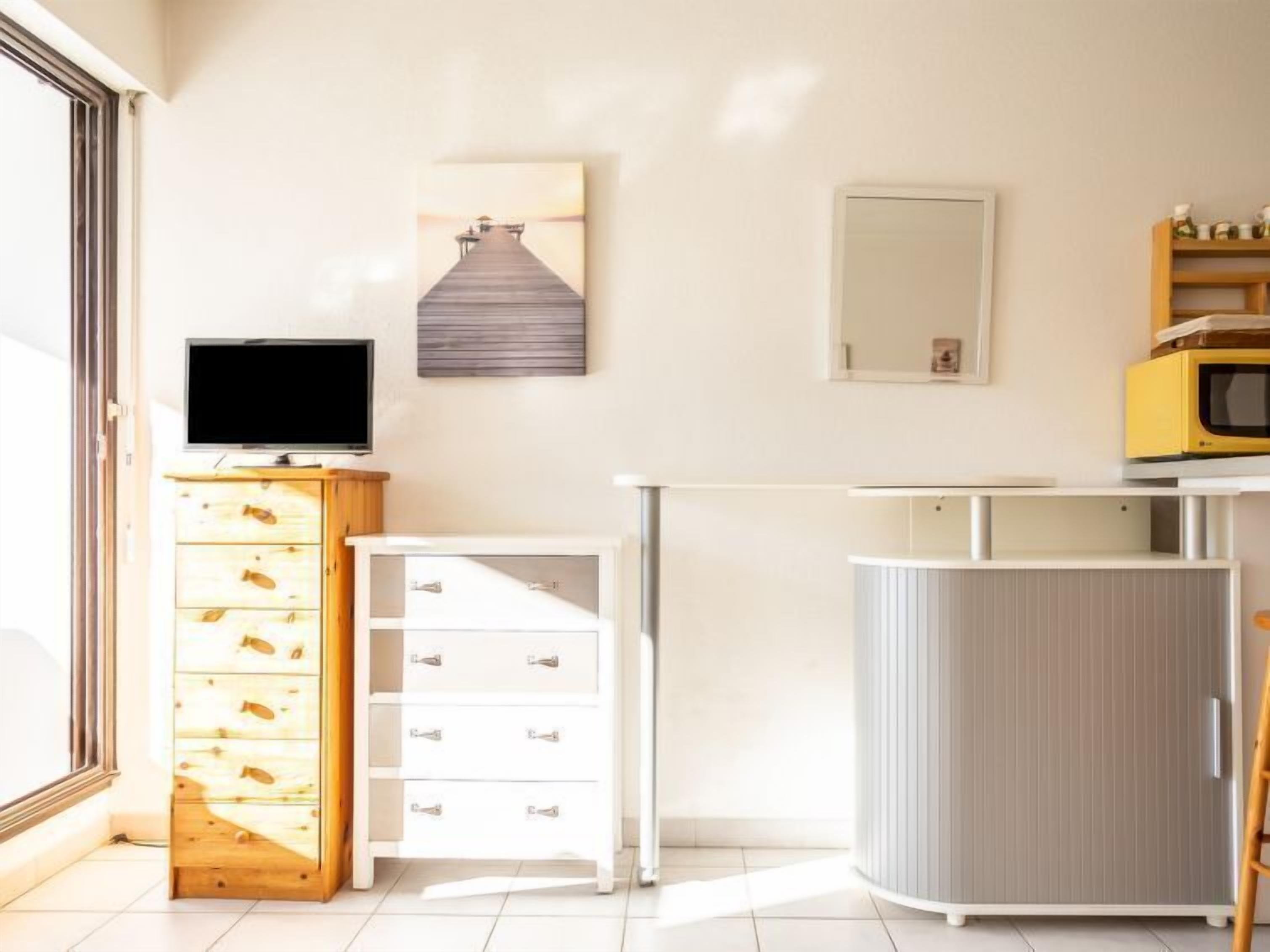 Cocina moderna con un armario de madera, un refrigerador blanco, un microondas y un televisor sobre un mueble de madera.