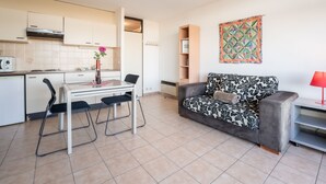 A compact living space with a kitchenette, a dining area with a table and chairs, a sofa, and a bookshelf. - Studio 705 with seaview by Interhome (Bredene)