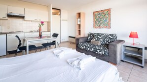 A modern hotel room with a bed, a desk, a chair, a sofa, and a small table with a lamp. - Studio 705 with seaview by Interhome (Bredene)