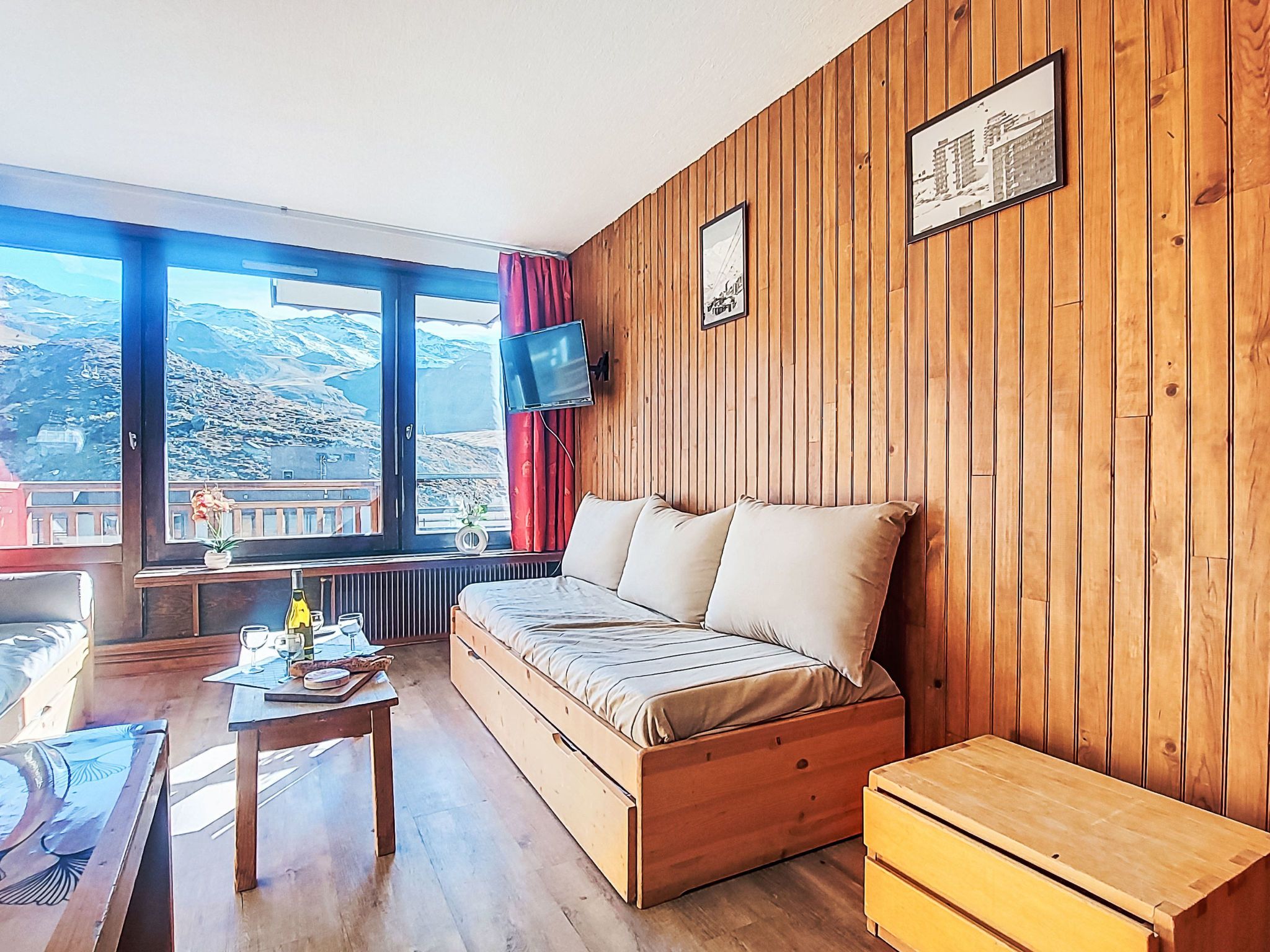 A room with a wooden wall, a sofa, a table with a bottle, and a TV mounted on the wall.