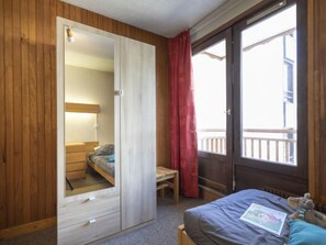 Un dormitorio con una cama litera, un armario de madera, un escritorio y una ventana con vistas a un balcón.