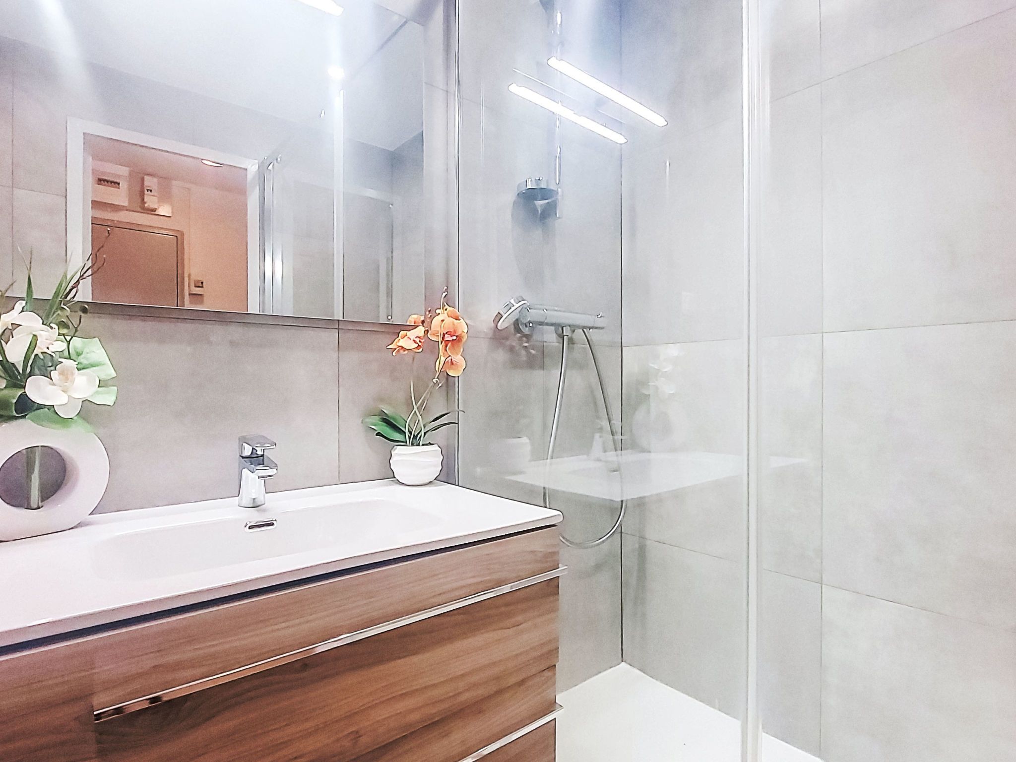 A modern bathroom with a glass shower enclosure, a wooden vanity, and a mirror above the sink.