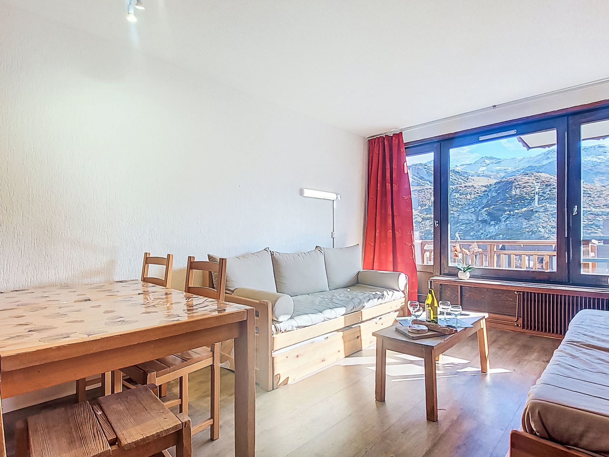 A room with a wooden dining table, a sofa, a small coffee table, and a window with a view of mountains.