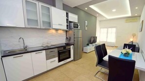A modern kitchen with white cabinets, a black countertop, and a built-in oven. There is a dining area with a table and chairs, and a TV mounted on the wall. - Apartment Niko 2 by Interhome (Omiš)