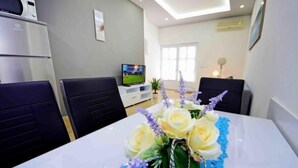 A modern dining area with a white table, blue table runner, and a centerpiece of yellow roses and purple flowers. There are black chairs around the table, a TV in the background, and a microwave on the left. - Apartment Niko 2 by Interhome (Omiš)