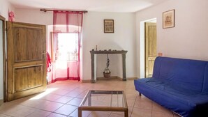 A living room with a blue sofa, a wooden door, a table with a lamp, and a window with a red curtain.