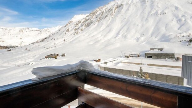 A snowy mountain landscape with a wooden balcony overlooking a snow-covered slope and buildings. - Le Slalom (Val Claret) by Interhome (Tignes)