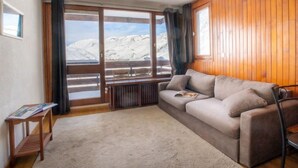 A cozy room with a large window offering a mountain view, a wooden wall, and a beige sofa. - Le Slalom (Val Claret) by Interhome (Tignes)