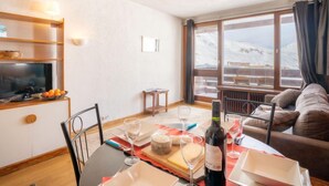 A cozy living room with a sofa, a dining table set for two, and a view of a snowy mountain landscape through large windows. - Le Slalom (Val Claret) by Interhome (Tignes)