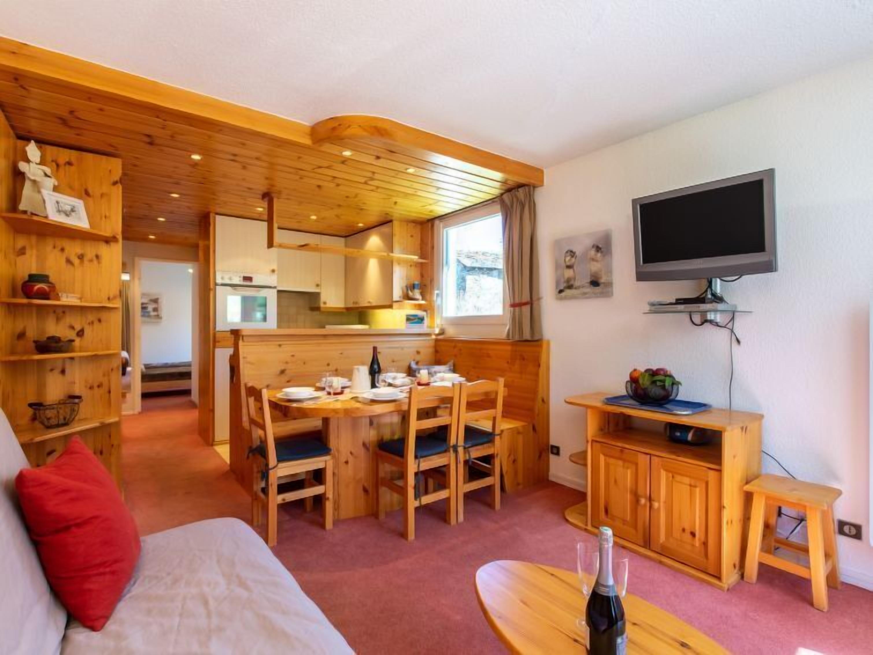 Um quarto aconchegante com uma cama, uma mesa de jantar com cadeiras, uma televisão e armários de madeira.