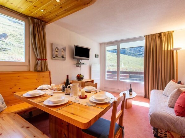 A cozy dining area with a wooden table set for four, a television on the wall, and a scenic view through the large windows.