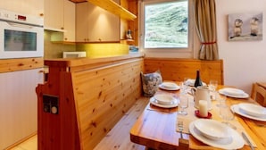 L’intérieur d’un chalet en bois comprend une cuisine, un coin repas et une fenêtre donnant sur un paysage montagneux.