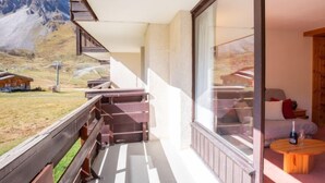 Un balcon doté d’une balustrade en bois, un petit coin salon avec une table et des chaises, et une vue sur une montagne et un bâtiment situé au loin.