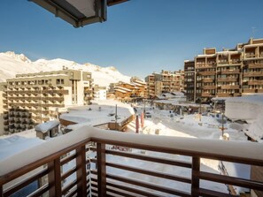 Un poble envoltat de neu a peu de muntanya, amb edificis de diversos pisos, incloent un hotel amb balcons i una zona de neu per esquiar.