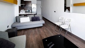 Un salon moderne avec un canapé gris, des chaises blanches et une table basse noire.